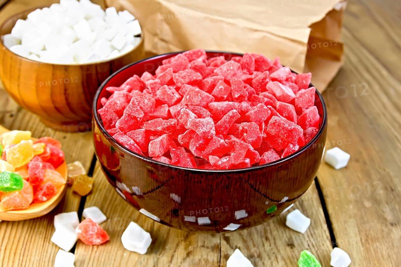 Candied papaya and coconut in bowls, colorful pieces of candied fruit in a spoon on a wooden boards background