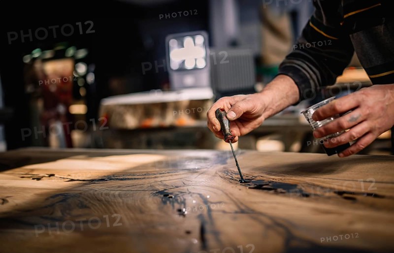 Close-up of hands expertly applying a tool to a wood surface under warm lighting in a shop setting