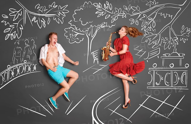 Love story concept of a romantic couple against chalk drawings background. Woman playing serenade on saxophone in a city park for her lover