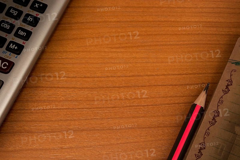 Wooden table with calculator in one corner and pencil and notebook in another