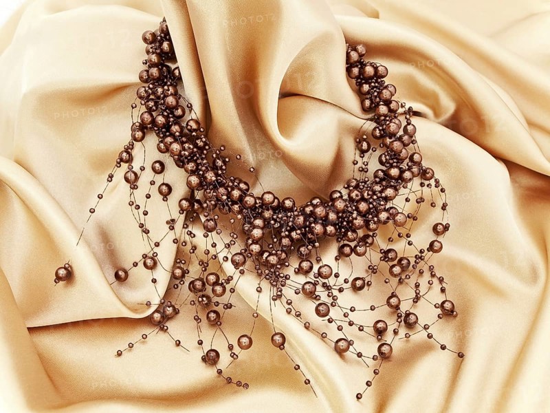 Fashion brown necklace in chaplet shape over golden textile background