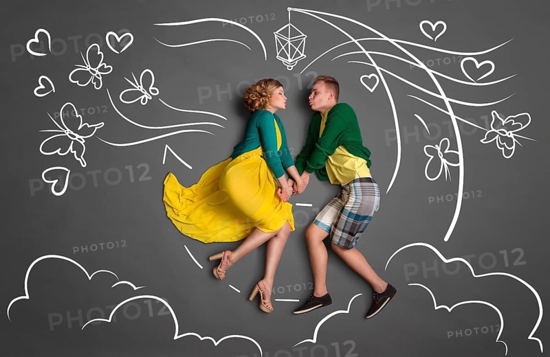 Happy valentines love story concept of a romantic couple sitting on the moon, holding hands and kissing against chalk drawings background of a night sky with butterflies
