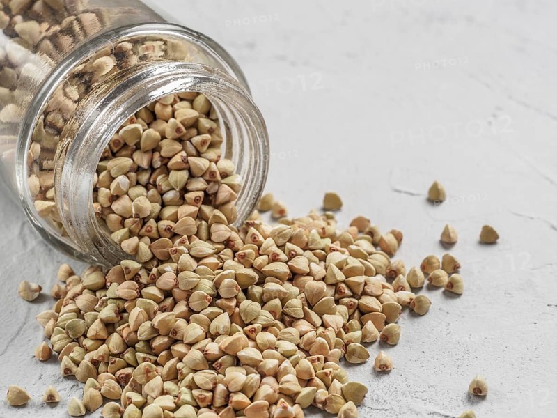 Raw green buckwheat in bank on gray background