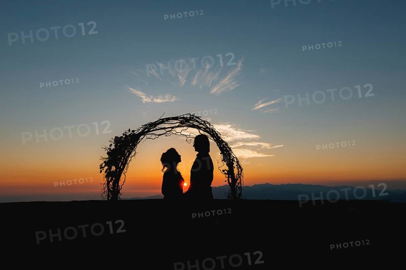 Silhouettes of bride and groom holding hands near the wedding arch at sunset at the wedding ceremony.