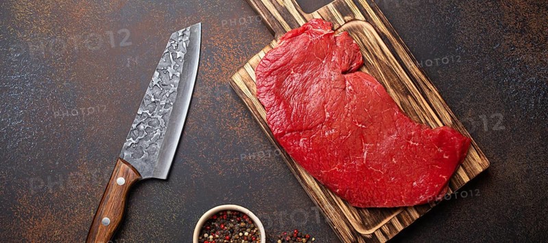 Raw uncooked top round beef steak on wooden cutting board with big kitchen knife and pepper on dark brown rustic stone background top view, cooking meat steak concept, food photography, food photography