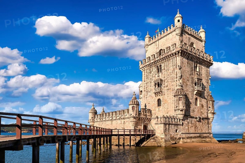 Belem tower and wooden bridge to it, Lisbon, Portugal at blue summer day sky with clouds. Medieval fort on Tagus river in late Gothic or Manueline style, UNESCO world heritage site, Age of Discoveries, tourist attraction, Portuguese seafaring history