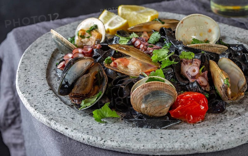 Food, Seafood black fettuccine fehttuchini. Black pasta with squids, octopus clams, mussels on stone plate. Gourmet dish