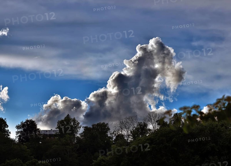 Threatening thundercloud grows behind a house into the blue sky, dramatic cloud formation, Upper Bavaria, Bavaria, Germany, Europe