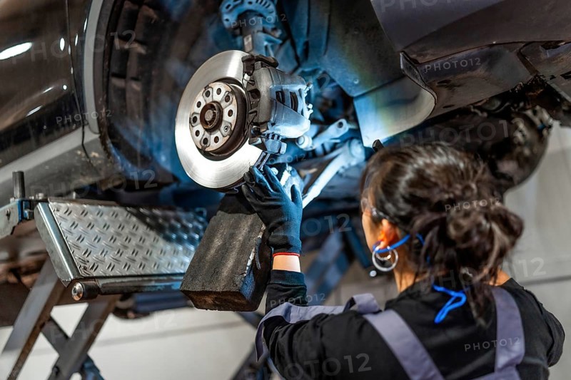 Female mechanic working under a car, inspecting and repairing brakes in a professional workshop