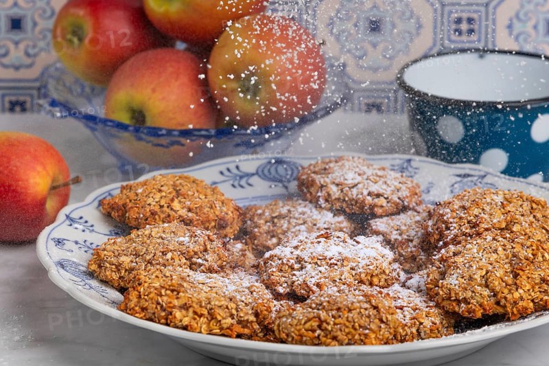 Freshly baked oat biscuits on a plate are sprinkled with sugar, apples in the background
