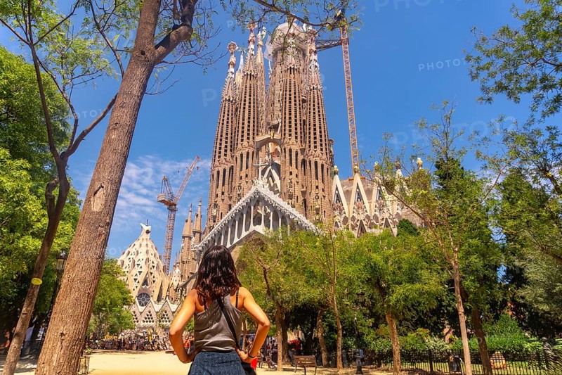 Young woman admiring the impressive sagrada familia basilica, a unesco world heritage site, during a sunny summer day in barcelona, catalonia, spain