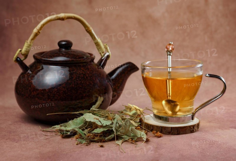 Glass cup with teapot and fresh linden leaves, infusion of lime blossom tea, medicinal plant with therapeutic properties