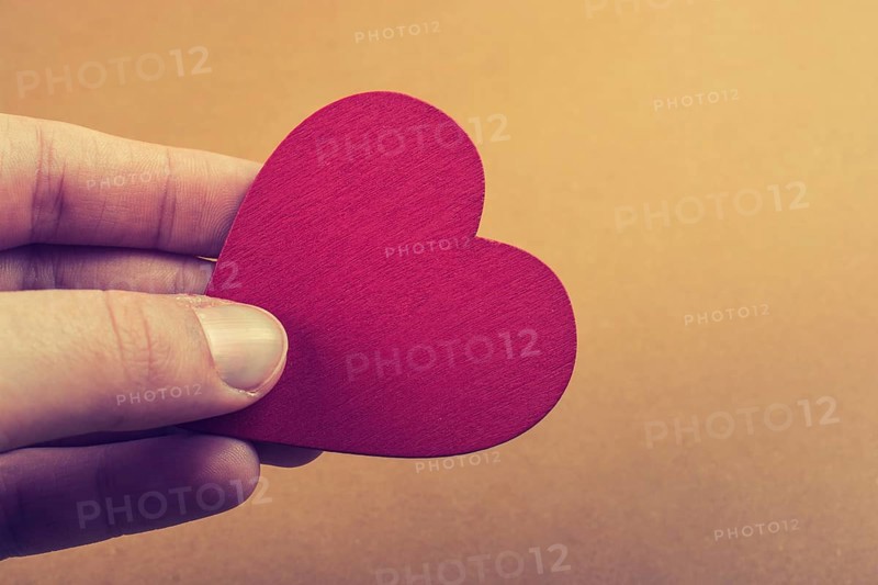 Red color heart shaped object in hand on dotted paper