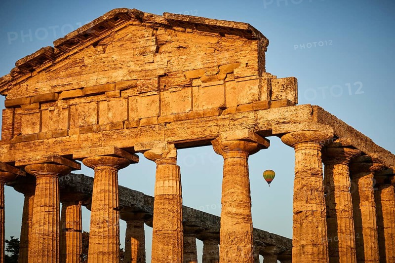 Sunset behind ancient columns of a temple with a clear sky, summer evening mood in Paestum, ancient town, 35 km south of Salerno.Founded by the Greeks around 600 BC, the city was given the name Paestum by the Romans in 274-273 BC.Important monuments from Greek and Roman times. The three large Doric temples are of particular importance. Europe, Italy. Campania. Salerno. Paestum