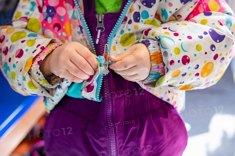 Close up shot on the hands of a kindergarten child struggling to latch and close the zipper of his winter coat before going outside in the wintertime