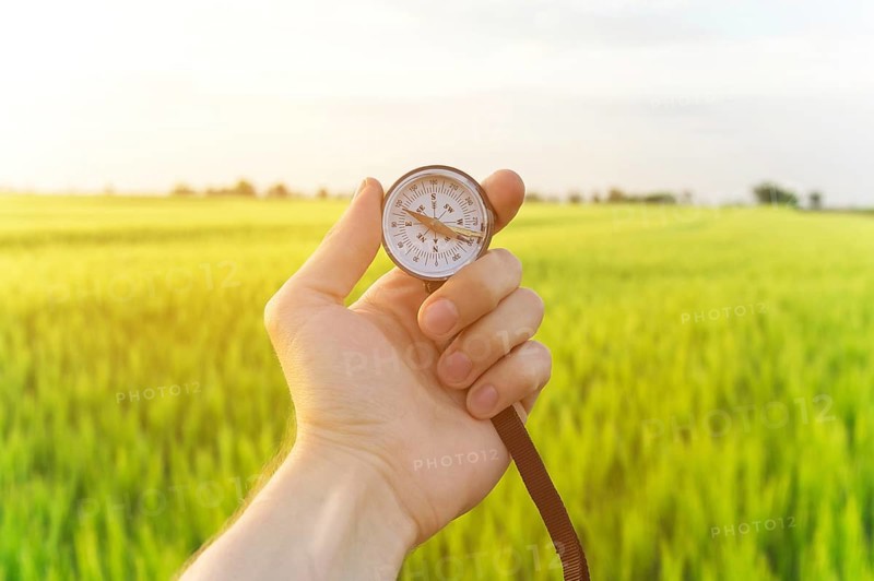 Finding a direction in nature on a wheat field. A man's hand holds a compass