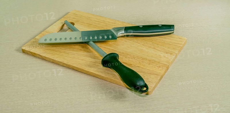 Santoku knife and honing steel on woodblock cutting board with light wood grain background