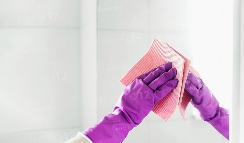 Cropped view of housekeeper woman hand in purple rubber gloves polishing mirror with pink cloth rag cleaner while cleaning bathroom at home. Housekeeping and cleaning service. Clean house, cleanliness