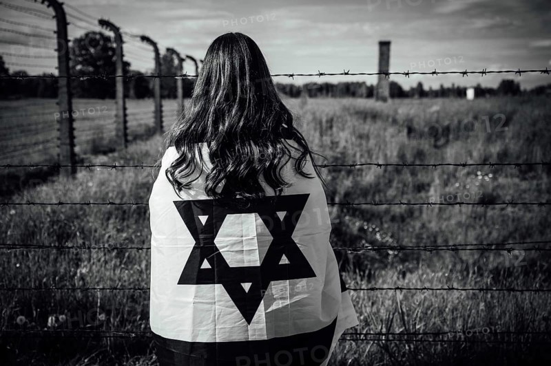 Jewish girl with Israeli flag by the fence of the concentration camp