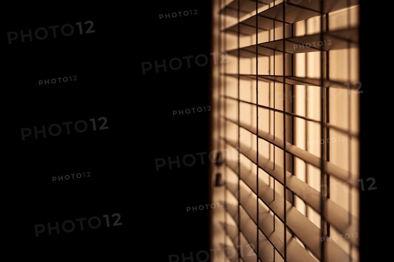 Horizontal shot of venetian blinds creating a moody and noir inspired atmosphere with light illuminating a dark room. Selective focus