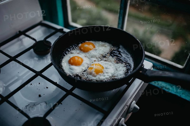 Frying pan with three eggs cooking on a gas stove beside a window