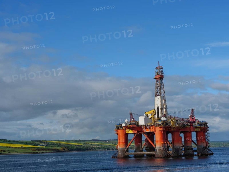 A single oil drilling platform sits in the calm sea with a slightly cloudy landscape behind it, drilling rig in red against a blue sky in the north sea, inverness, Scotland, United Kingdom, Europe