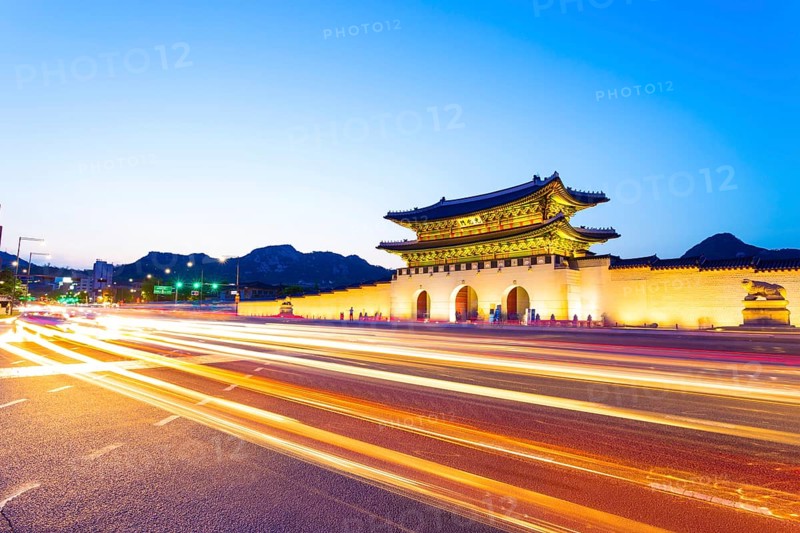 Colorful streaking headlights of cars passing in front of lighted gate of Gwanghuamun, entrance to historic Gyeongbokgung Palace at twilight in downtown Seoul, South Korea. Horizontal