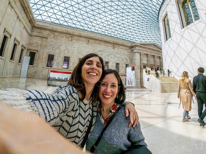 Two joyful female tourists capturing a selfie while enjoying their time in the stunning great court of the british museum in london
