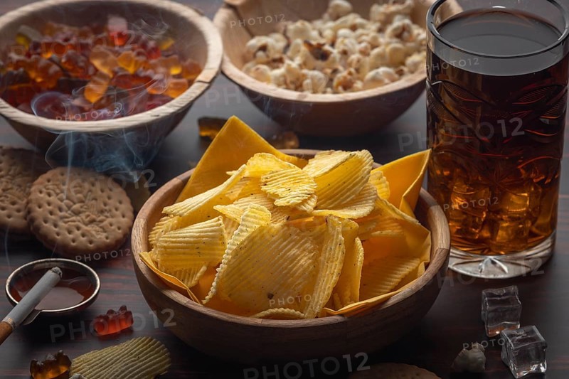 Crisps, popcorn, gummy bears, biscuits and a drink next to a cigarette