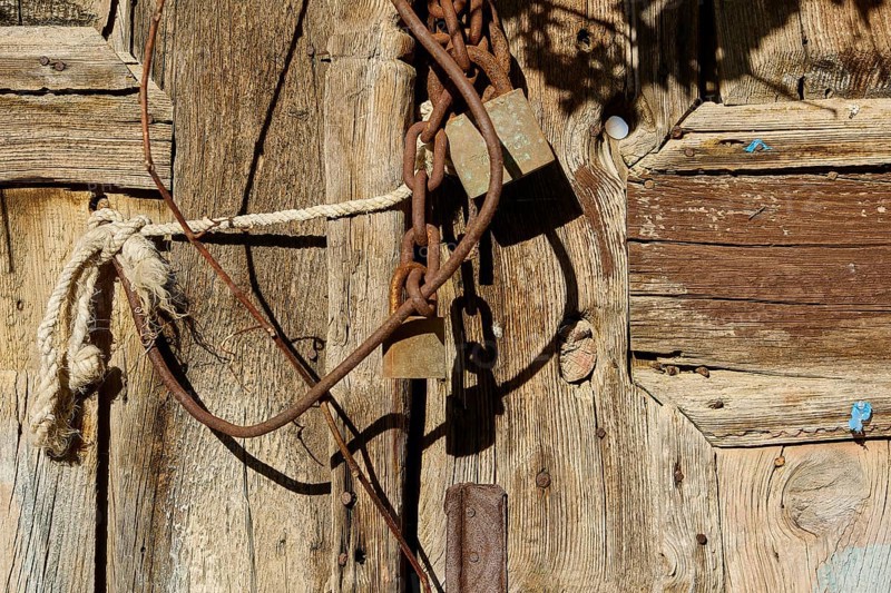 Old wooden door with rusty chains and locks, weathered in the sunlight, Symi Town, Symi, Dodecanese, Greek Islands, Greece, Europe
