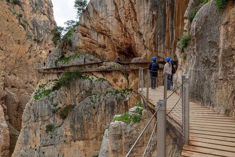 People with helmets walking on the wooden path Caminito del Rey along a rocky cliff, Malaga, Spain, Europe