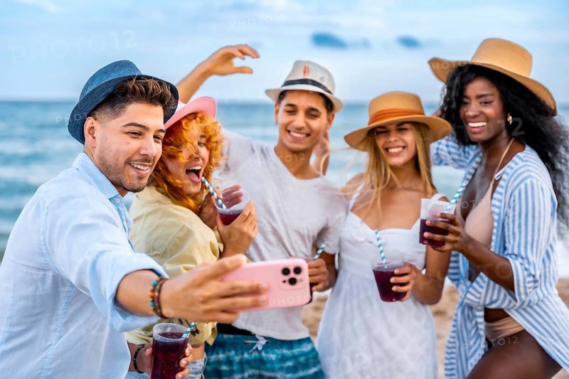 Multi ethnic friends taking selfie on beach while drinking juice, enjoying summer vacation together