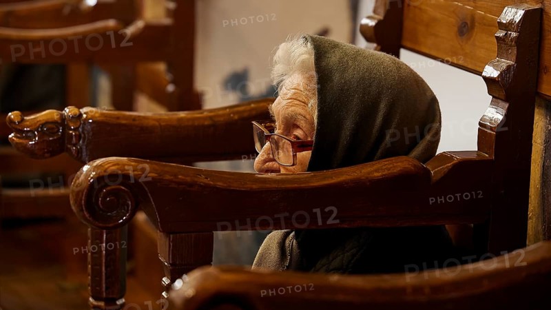 An elderly woman with a hood, sitting in a chair, deep in thought, Easter 2025, Church of the Dormition of the All-Holy God Bear, Kimisis tis Theotokou, Asklipio, Rhodes, Dodecanese, Greek Islands, Greece, Europe