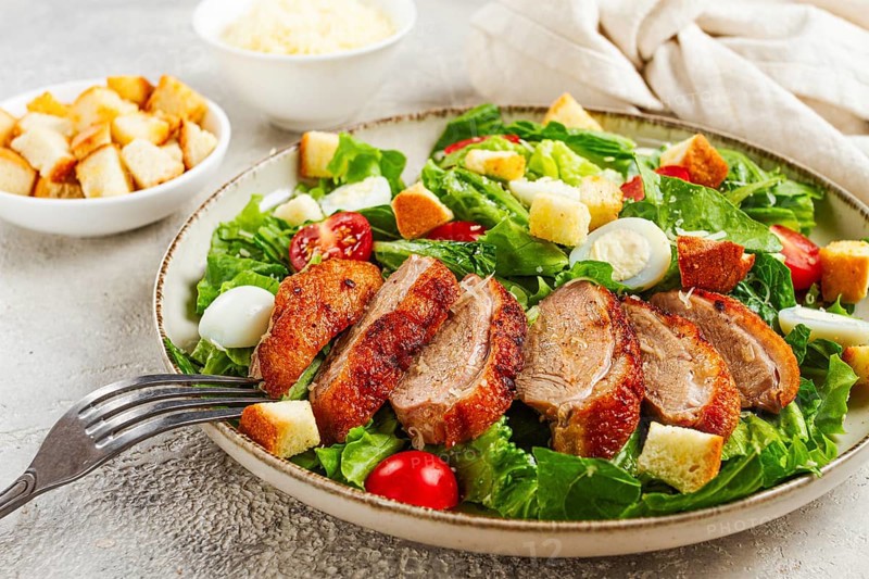 Caesar salad, with duck breast, on a light plate, on a light background, homemade, no people