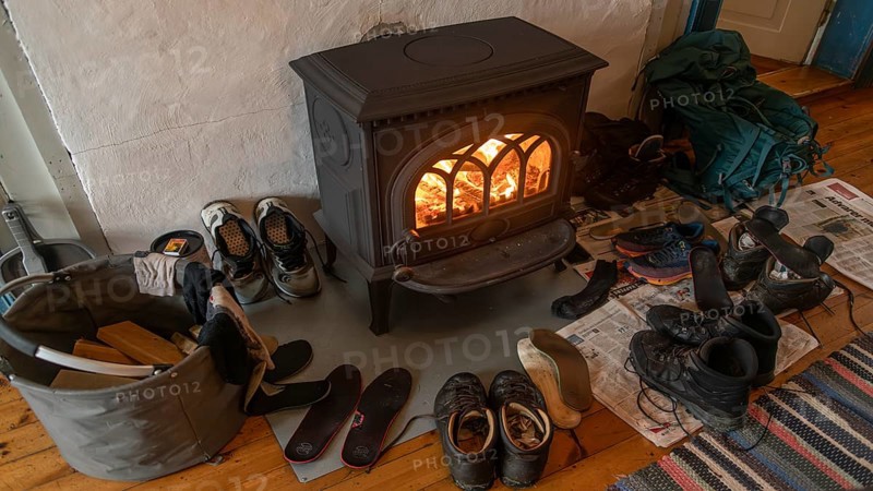Drying wet hiking boots in front of a burning wood-burning stove, Fokstugu farm, Fjellstue, pilgrims' accommodation, mountain hut, Olavsweg, Olavsleden or Pilgrimsleden, Dovrefjell-Sunndalsfjella National Park, Norway, Europe