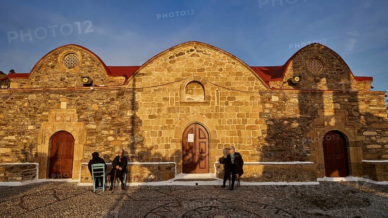 Historic stone church under the evening sun with people sitting in front of it, Easter 2025, Church of the Dormition of the All-Holy God Bear, Kimisis tis Theotokou, Asklipio, Rhodes, Dodecanese, Greek Islands, Greece, Europe