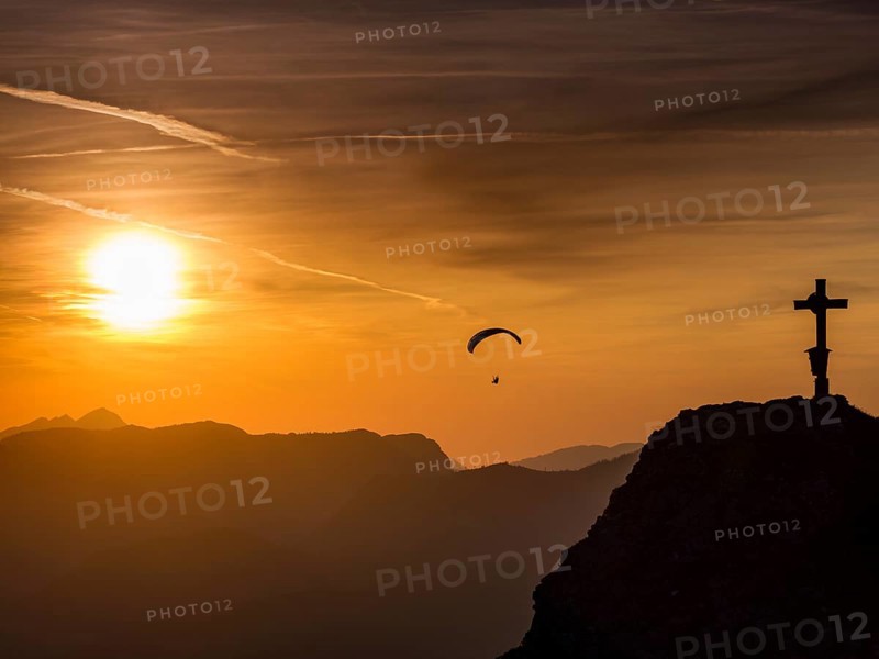 Paraglider flying next to the summit cross of the small Jenner at sunset, Reiteralpe in the background, Berchtesgaden National Park, Schönau am Königssee, Upper Bavaria, Bavaria, Germany, Europe