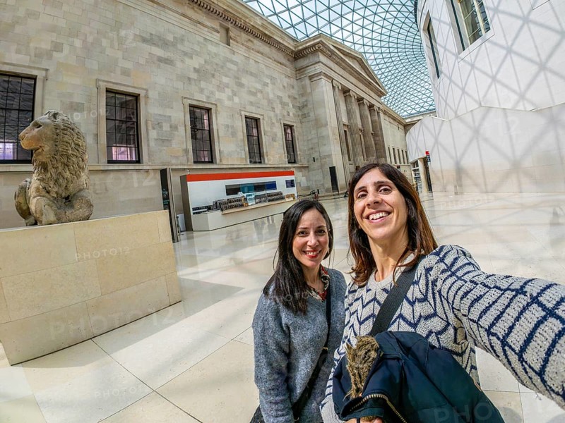 Two happy female tourists are taking a selfie with a fisheye lens at the british museum's great court in london, uk
