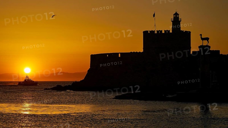 A boat glides in front of the silhouette of a fortress in the warm sunrise, dawn, Fort of Saint Nikolaos, Mandraki harbour, Rhodes town, Rhodes, Dodecanese, Greek Islands, Greece, Europe