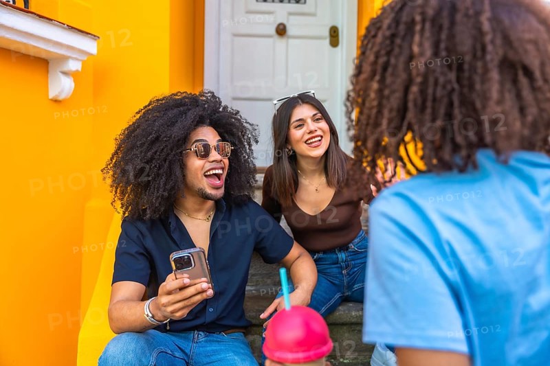 Three cheerful friends enjoying a lively conversation and refreshments while sitting on vibrant steps, creating a joyful and social atmosphere