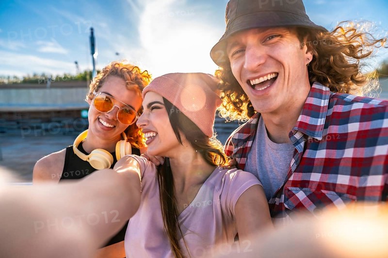 Three cheerful young friends taking a selfie outdoors, soaking up the sun and enjoying a vibrant day in the city together