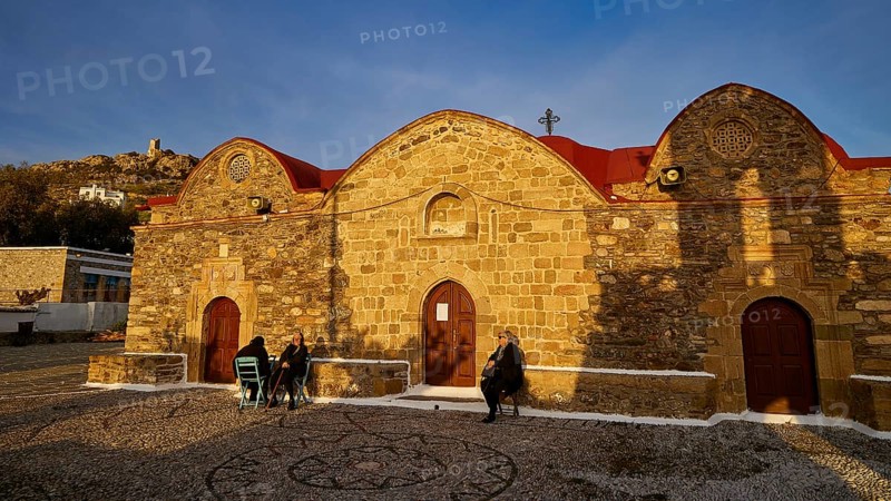 Stone church with rounded roofs and some people walking along in the evening light, Easter 2025, Church of the Dormition of the All-Holy God Bear, Kimisis tis Theotokou, Asklipio, Rhodes, Dodecanese, Greek Islands, Greece, Europe