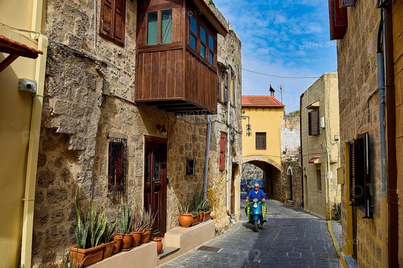 Narrow historic alley with a scooter driver and flower pots on a stone building, Rhodes Old Town, Rhodes, Dodecanese, Greek Islands, Greece, Europe