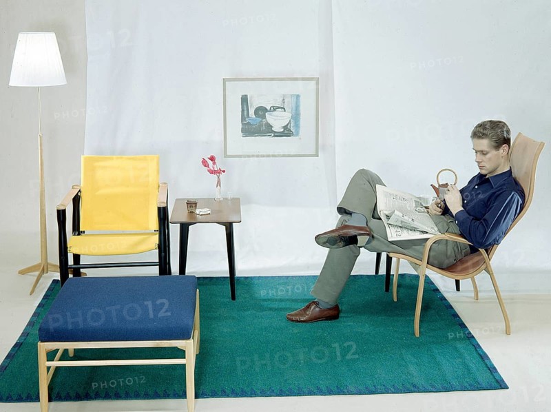 In the 1950s 1960s. A man is sitting comfortably in an armchair reading the newspaper and having a cup of tea and a cigarette. The furniture are made of wood and typical of the late 1950s early 1960s style. Sweden 1958 Conard ref BV109-6