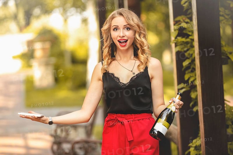 Happy young attractive white woman laughing joyfully, talking on the phone, holding a bottle of champagne and calling for a party. emotions lifestyle leisure relaxation positive communication