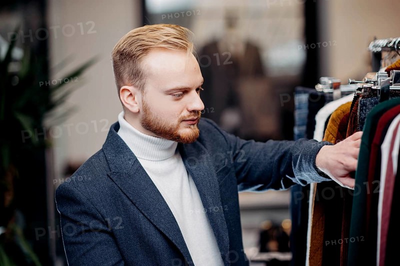 A focused man browses jackets in a clothing store, conveying a sense of style and interest