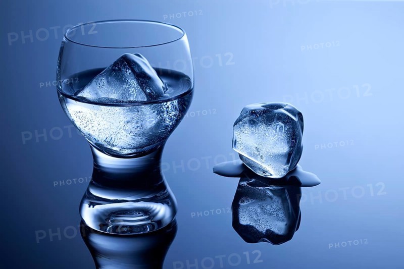 An elegant shot glass with vodka and ice and a melting ice cube on a reflective surface
