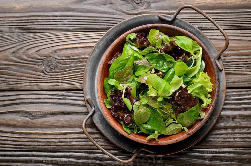 Top view at clay dish with green and violet lettuce, lamb's lettuce salad with oregano flowers on vintage metal tray