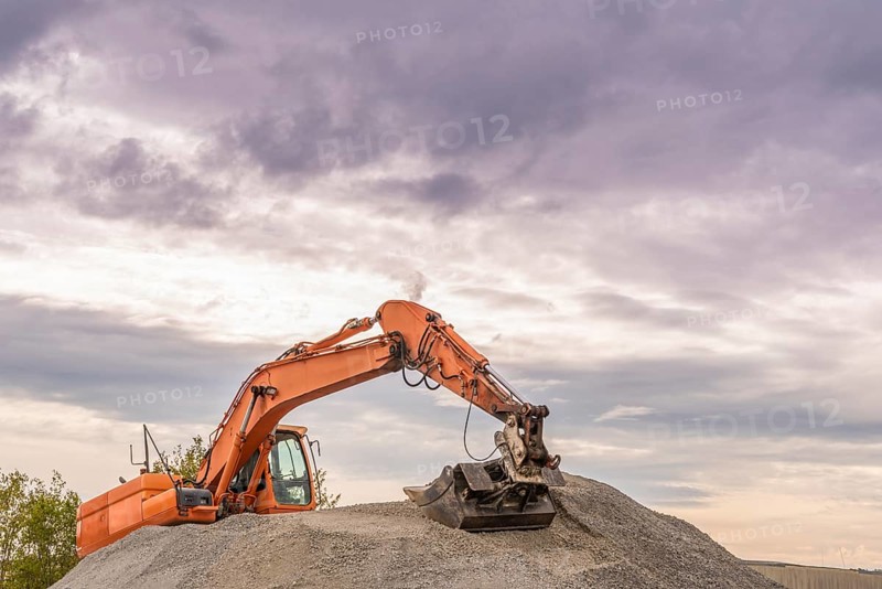 Heavy orange excavator with big bucket working on top of a ballast pile
