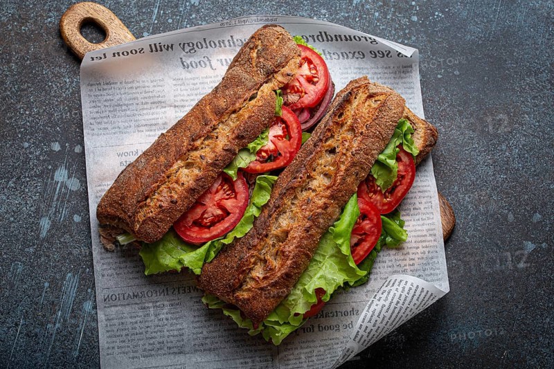 Two dark ciabatta sandwiches with green salad, ripe red tomatoes, onion and tuna on rustic concrete stone background top view. Vegetable vegetarian sandwiches, healthy snack or lunch, food photography, food photography